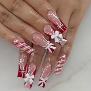 Long red French tip Christmas press on nails worn on hand featuring 3D white bow charms, candy cane stripes, hand-painted snowflake starburst line art and sheer pink base with white swirl details