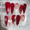 Red and white luxury Christmas press on nails with cable knit texture, oversized ruby gem cascade, broken glass gem effect, 3D white bow, snowflake and gold Christmas bell charm in clear nail box