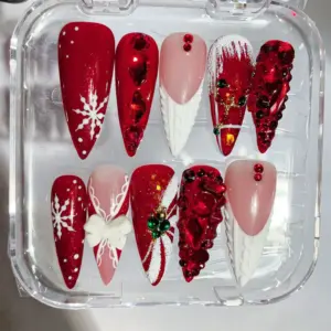 Red and white luxury Christmas press on nails with cable knit texture, oversized ruby gem cascade, broken glass gem effect, 3D white bow, snowflake and gold Christmas bell charm in clear nail box