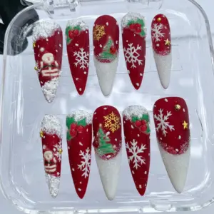 Red Christmas press on nails with 3D sculpted snow tips, hand-painted Santa Claus, Christmas tree, white snowflakes, holly berries and gold star accents in clear nail box