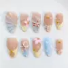 Nude beach press on nails with 3D realistic brown starfish charm, soft pink 3D floral bloom with gold bead, sculptured shell fan relief in blue-nude ombré and champagne tones, bubble gel water droplet texture on powder blue base, gold mini starfish charms, and pearl bead accents on summer fake nails