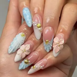 Elegant beach press on nails worn on hand featuring 3D sculpted blue seashell with gold charm, blush pink 3D flowers, pearl beads, and ocean water marble accent on nude pink fake nails