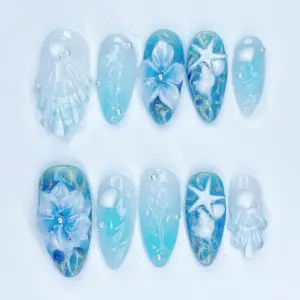 Blue ocean press on nails with 3D sculptured white seashell, 3D starfish charm, white 3D floral bloom with pearl bead, hand-painted seahorse and seaweed line art, gold shimmer base, and silver rhinestones on aqua summer fake nails