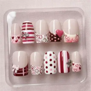 Short French tip Valentine's Day press on nails with bow charm, stripe, polka dot, plaid, scrollwork swirl and heart designs in red pink and nude displayed in a clear nail box