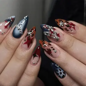 Grunge Y2K press on nails worn on hand with navy matte base, red stars, 3D silver safety pin charm, cross charm, burnt orange leopard print, dalmatian spots, and silver bead accents