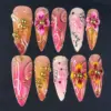 Hot pink and coral orange ombré press on nails with 3D fuchsia and golden yellow floral blooms, clustered gold ball beads, white swirl brushstrokes, gold vine lines, silver rhinestones, and dark wine dot accents on long summer fake nails