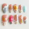 Nude pink press on nails with 3D tropical flower in cream and yellow, 3D hot pink floral bloom with pearl center, gold starfish and shell charms, transparent shell fan relief, bubble gel texture, and teal glitter accent on summer fake nails