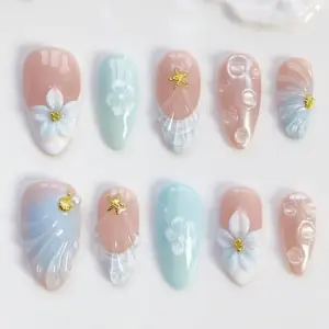 Ocean-inspired press on nails with 3D white flowers, gold starfish charms, pearl shell details, and soft pink-mint ombré on glossy fake nails