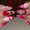 Red and pink ombre Valentine's Day press on nails with heart outlines, rhinestone gems and pearl details worn on hands