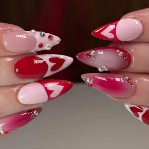 Red and pink ombre Valentine's Day press on nails with heart outlines, rhinestone gems and pearl details worn on hands