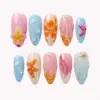 Pastel Ocean Press On Nails | 3D Starfish Plumeria Shell Summer Fake Nails | SE61 7 Pastel summer press on nails with 3D yellow-orange plumeria bloom and crystal bead, orange 3D starfish on peach base, hot pink starfish on powder blue, gold starfish with pearl beads on white shell nail, clear bubble gel water droplets on aqua, hand-painted hibiscus, and shell fan relief in orange-peach and blue tones on summer fake nails