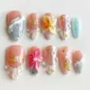 Peach ocean press on nails with 3D cream and yellow tropical flower bloom with gold center, 3D hot pink floral with pearl center, gold starfish and scallop shell charms, shell fan relief with pearl beads, bubble gel wave texture, silver foil aqua glitter accent nail, and soft grey-blue lace texture on summer fake nails