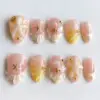 Peach aurora press on nails with 3D transparent shell fan, gold starfish charm, milky white floral bloom, gold bead accents, and warm blush-peach ombré on glossy fake nails