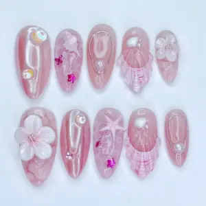 Pink aurora chrome press on nails with 3D white floral bloom and crystal bead center, translucent pink shell fan relief with fuchsia stripes, iridescent AB bubble gems, fuchsia star charms, rose gold teardrop wire frame with floating pearl, and pink starfish ocean texture on summer fake nails