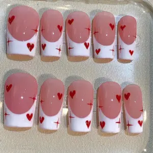 Soft pink French tip press on nails with red hearts and sparkle star accents for Valentine's Day