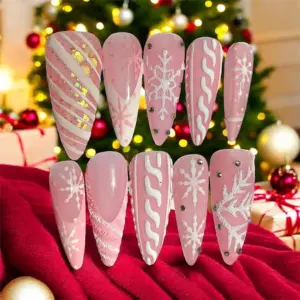 Blush pink Christmas press on nails with white glitter snowflakes, holographic gold stripe glitter, raised 3D white swirl texture and AB rhinestone accents against Christmas tree backdrop
