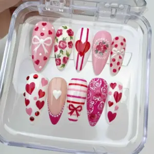 Coquette Valentine's Day press on nails with roses, bows, hearts, stripes, pearls and rhinestones in pink white and magenta displayed in a clear nail box