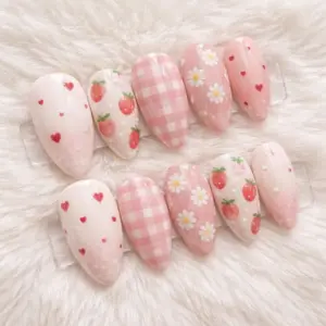 Kawaii blush pink press on nails with strawberry, daisy flower, pink gingham plaid and mini heart designs displayed on white fur