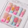 Vibrant tropical press on nails with 3D yellow sunflower and pink polka-dot flowers, white hibiscus hand-painted art, rhinestones, and pink-blue ombré on long fake nails in a clear nail box