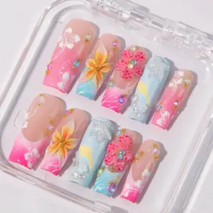 Vibrant tropical press on nails with 3D yellow sunflower and pink polka-dot flowers, white hibiscus hand-painted art, rhinestones, and pink-blue ombré on long fake nails in a clear nail box